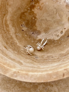 Detailed view of 925 sterling silver bow earrings with round white pearls on stone