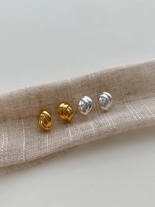 Gros plan de boucles d'oreilles nœuds minimalistes dorées et argentées sur ruban en lin