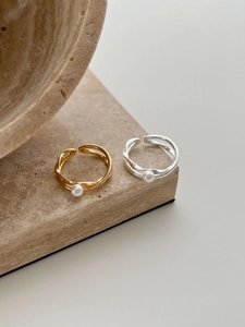 Detail view of gold and silver crossover pearl rings on a travertine stone pedestal