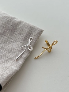 Gros plan de boucles d'oreilles nœuds en or et argent sur fond de tissu en lin gris