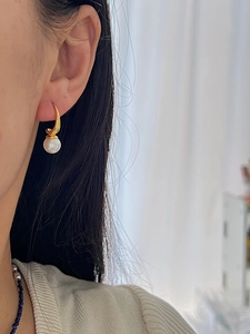 Close-up of elegant C-shaped pearl drop earrings with gold hooks on a model