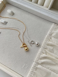 Macro detail of minimalist S925 silver OT buckle necklaces with smooth metal sphere pendants