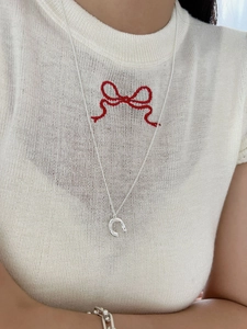 Detail of silver horseshoe pendant necklace and ball-hook bracelet on white knitwear