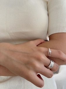 Close-up of minimalist pearl cross ring and wide lava texture silver ring on hand