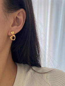 Close-up of golden hollow heart drop earrings worn by a model for a vintage look