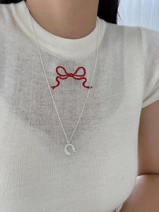 Close-up of a silver horseshoe pendant necklace on a model with white knitwear