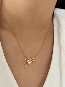 Gros plan d'un collier avec pendentif nœud doré et perle sur le cou d'une femme