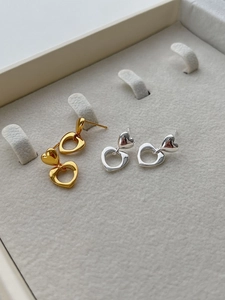 Close-up of polished gold and silver hollow heart earrings on grey velvet jewelry tray