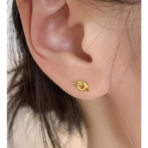 Minimalist golden knot stud earrings in 925 sterling silver worn on a model's ear lobe