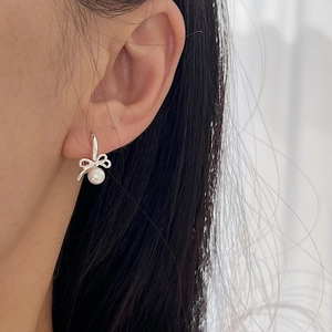 Elegant 925 sterling silver bow earrings with white pearls worn by a model in a side view