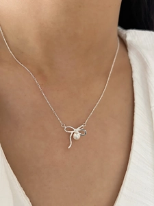 Gros plan d'un collier nœud en argent S925 avec perle porté sur la clavicule d'un mannequin