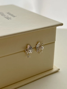 Detailed view of silver folding fan earrings with white pearls on a display box