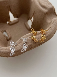 Detail of S925 sterling silver bow earrings in gold and silver finish on a rustic tray