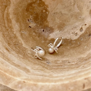 Elegant 925 sterling silver bow earrings with round white pearls in marble dish