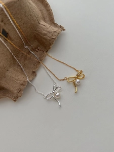 Détail de colliers en perles avec nœud argent et or sur un fond gris minimaliste