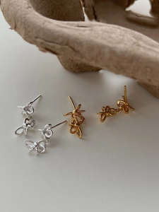 Detailed view of silver and gold bow earrings on a minimalist stone backdrop
