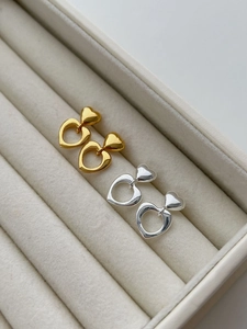 Close-up of gold and silver hollow heart-shaped earrings on beige velvet tray