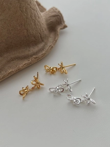 Detailed view of elegant gold and silver ribbon bow earrings in a minimalist setting