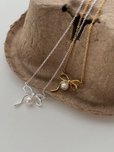 Détail de colliers nœud argent et or avec perles élégantes présentés sur support papier