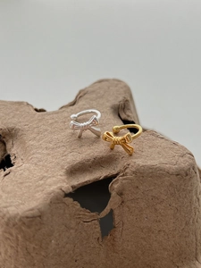 Macro detail of elegant silver and gold bow ear cuffs on textured organic background