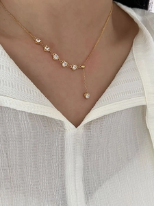 Detail of elegant gold heart zircon necklace worn on a white shirt showing the design