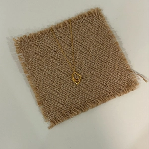 Goldene Halskette mit Doppelherz-Anhänger auf braunem Leinen, minimalistischer Schmuck
