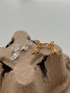 Detailed view of silver and gold ribbon bow stud earrings on a vintage pulp texture