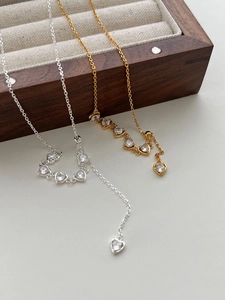 Detailed view of silver and gold heart pendant necklaces on a dark wood jewelry box