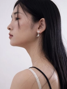 Detail shot of a delicate silver bow earring worn on a model's ear for an elegant style