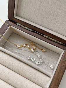Detail of silver and gold heart necklaces with zircon inlay in a walnut jewelry box