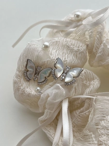 Détail de boucles d'oreilles papillon en nacre et zircons sur fond de satin blanc doux