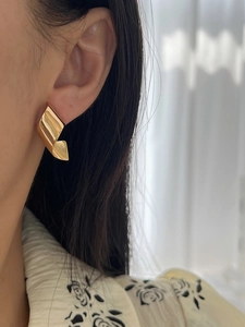 Close-up of elegant gold twisted ribbon earrings on model in natural indoor light