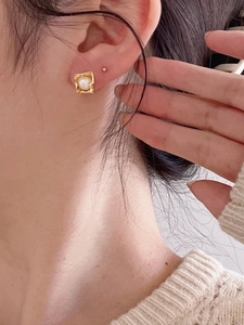 Close-up of vintage square gold earrings with white pearls on a model wearing knitwear