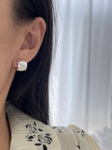 Close-up of a high-polished silver C-shaped earring worn on the ear showing size and texture