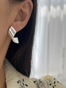 Close-up of twisted silver ribbon hoop earrings with metallic foil texture on model
