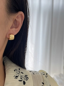 Close-up of a wide polished gold C-shaped hoop earring worn by a model in soft light