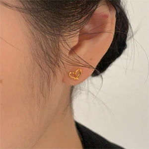 Gros plan d'une boucle d'oreille cœur évidée dorée minimaliste sur le lobe