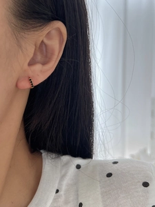 Close-up of a small gold huggie earring with three inlaid round black gemstones