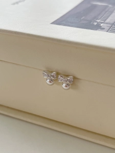 Close-up of bow-knot pearl earrings with sparkling crystals in a beige jewelry box