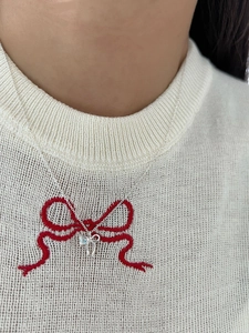 Macro shot of silver bow pendant with heart moonstone on a white knitted sweater
