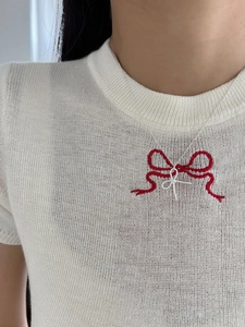 Close-up of sterling silver bow necklace with micro-pave crystals on a white knit top