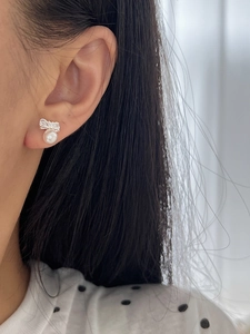 Close-up of 925 silver bow stud earrings with small zircon stones and white pearls