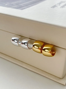 Macro detail of polished gold and silver C-shape hoop earrings on a leather box