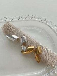 Detail of twisted ribbon silver earrings in gold and silver finish on rustic linen