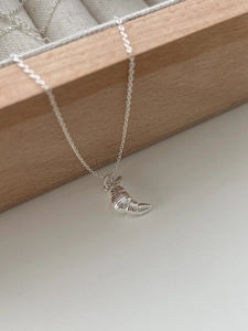 Detailed view of silver croissant pendant necklace hanging on a light wooden jewelry box