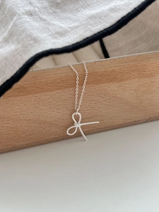 Macro detail of a silver bow necklace with twisted rope design hanging on wood