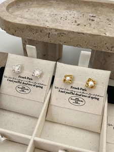 Close-up of pearl stud earrings in gold and silver irregular frames on display card