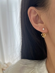 Détail de boucles d'oreilles cœurs dorées portées par un mannequin sur fond de rideau blanc