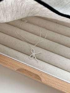Macro shot of silver bow pendant with twisted texture in a velvet wooden jewelry box