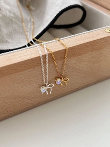 Detail of moonstone bow necklace in gold and silver finish resting on a wooden box